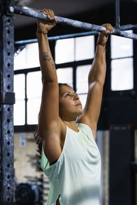 Strong hispanic female in activewear doing pull up on bar during intense fitness training in sports club