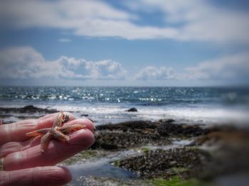 Hand holding sand at beach against sky