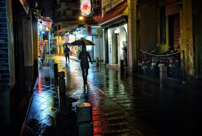 People walking on wet street in illuminated city at night