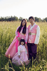 Korean family in national costumes is stand in a field at sunset in the grass
