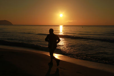 Silhouette man jogging on beach at sunset
