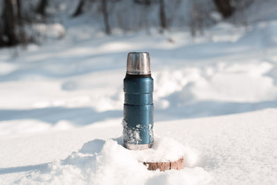 Metal blue thermos standing on a snowy tree stump in a winter forest on a sunny day