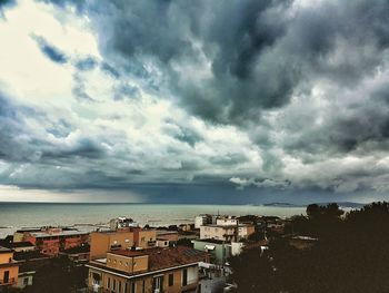 Houses in sea against cloudy sky