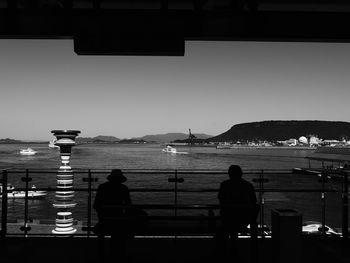 People sitting by sea against clear sky