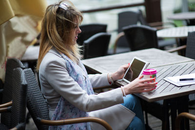 Woman using mobile phone while sitting on table at cafe