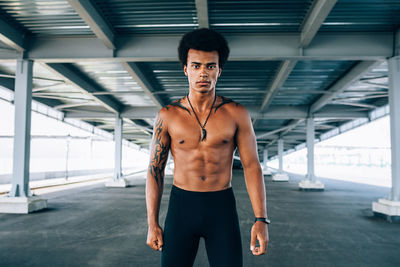 Portrait of shirtless man standing under bridge 