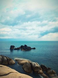 Scenic view of rocky seaside against cloudy sky