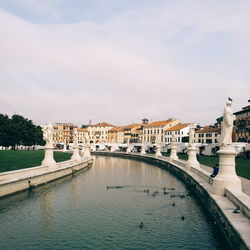 Bridge over river by buildings in city against sky