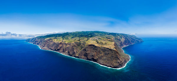 Aerial view of island amidst sea against blue sky