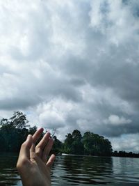 Close-up of hand by lake against sky