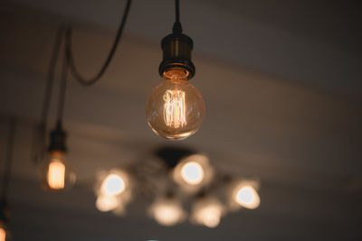 Low angle view of illuminated light bulb hanging from ceiling