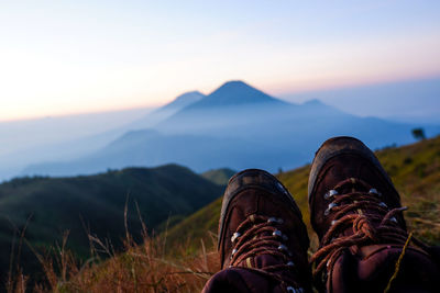 Low section of person relaxing on land against sky during sunset