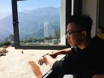 Side view of young man sitting on table against window