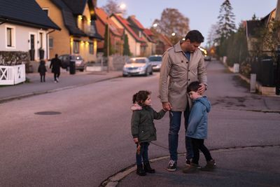 Father consoling sad son while holding hands with daughter on footpath during sunset