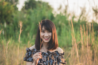 Portrait of young woman holding grass while standing on field