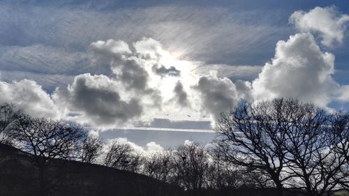 Low angle view of bare trees against cloudy sky