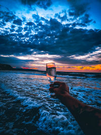 Man holding glass of sunset over sea