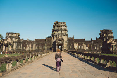 Rear view of woman walking towards temple against blue sky
