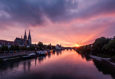 View of river amidst buildings against sky during sunset