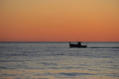 Silhouette boat in sea against orange sky