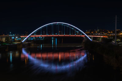Bridge over river in city against sky at night