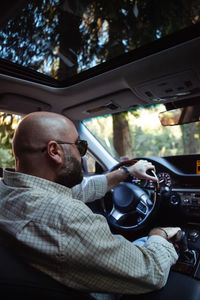 Brutal bald bearded middle-aged man drives a car