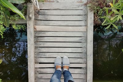 Low section of woman standing on wooden footbridge over river