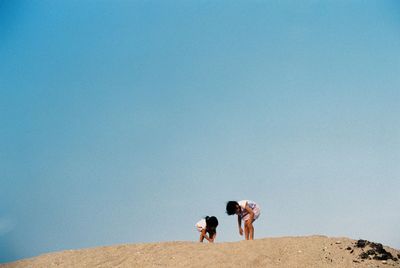 Siblings on sand at beach against clear sky