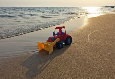 Toy car on beach against sky during sunset