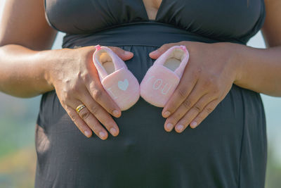 Midsection of pregnant woman holding baby booties on abdomen