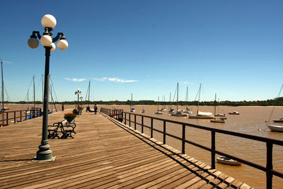 Street lights on pier by sea against clear sky