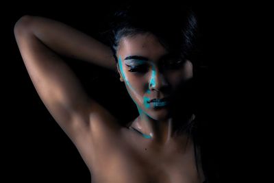 Close-up of shirtless woman with face paint against black background