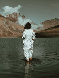 Rear view of man standing in lake against sky