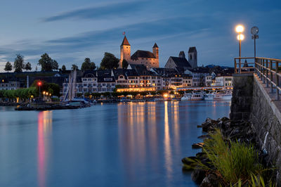 Illuminated castle by lake against sky at dusk