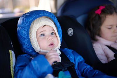 Siblings sitting in safety chairs in the back seat of a car