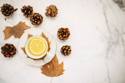 Top view of a cup of lemon tea surrounded pine cones and autumnal maple leaves. focus on lemon.