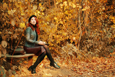 Full length of young woman sitting on autumn leaves