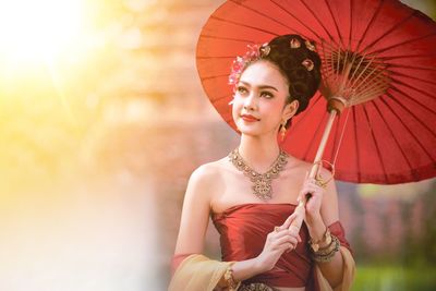 Young woman in traditional clothing with umbrella standing outdoors