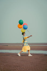Full length portrait of young woman holding colorful balloons at beach