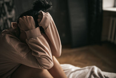 Rear view of woman sitting on bed at home