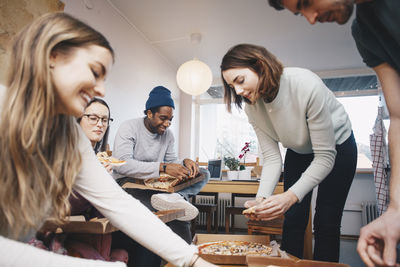 Happy young friends eating pizza in college dorm room