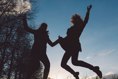 Low angle view of silhouette female friends jumping against sky during sunset