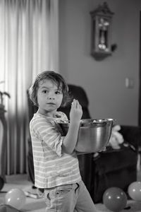 Side view of boy holding popcorn in large bowl at home