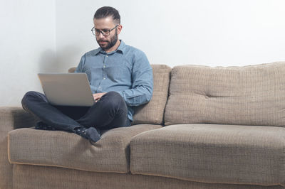 Full length of man using laptop while sitting on sofa at home