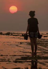 Rear view of woman standing on beach during sunset
