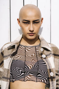 Confident young woman with shaved head in front of wall