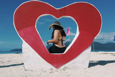 Woman with red umbrella at beach against sky