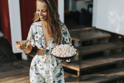 Smiling young woman carrying popcorn and peanuts