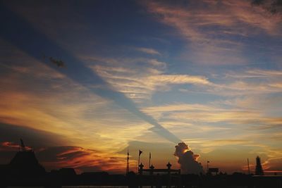 Silhouette factory against sky during sunset