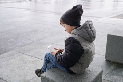 Boy using phone while sitting on seat during winter
